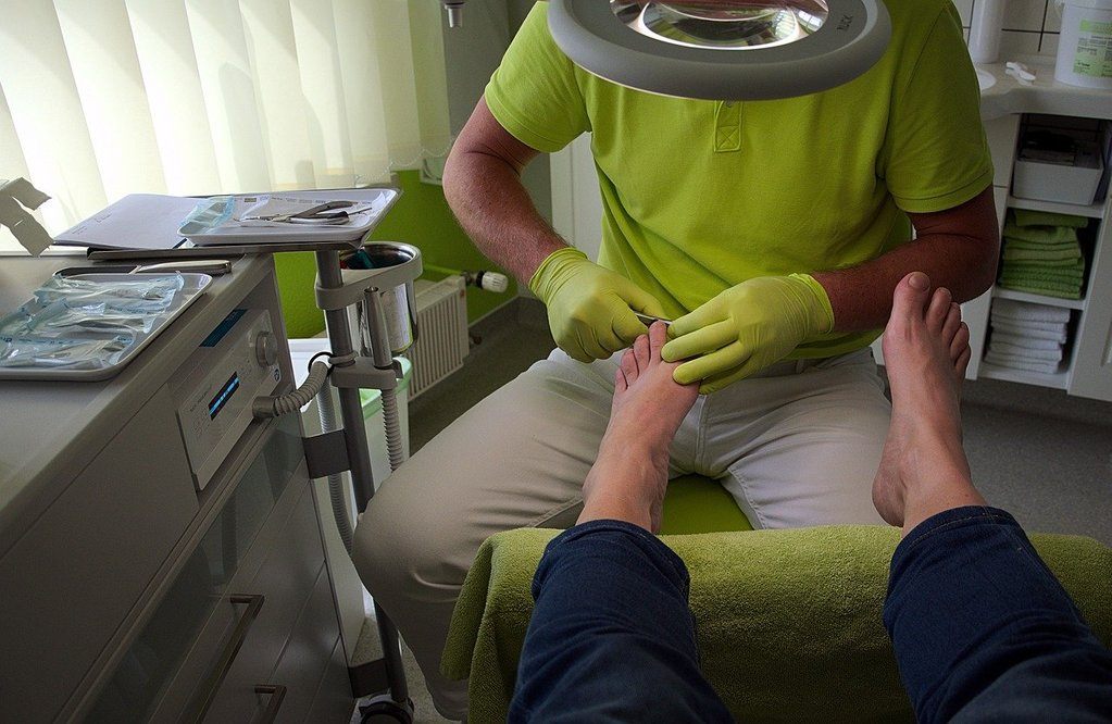 man in a green polo doing nail care in a doctor's office